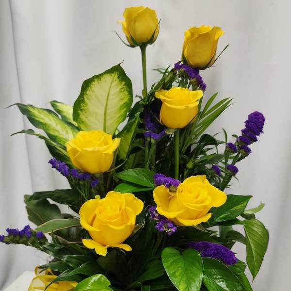 Yellow roses and purple filler flowers arranged in a decorative vase