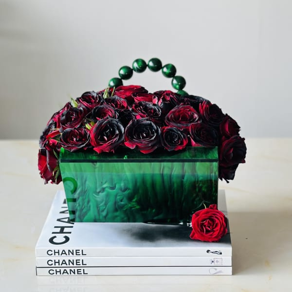 Red roses arranged in a green handbag-shaped box on stacked Chanel books