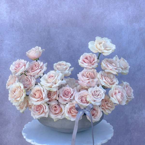 Arrangement of pale pink and white roses in a shallow bowl with a ribbon