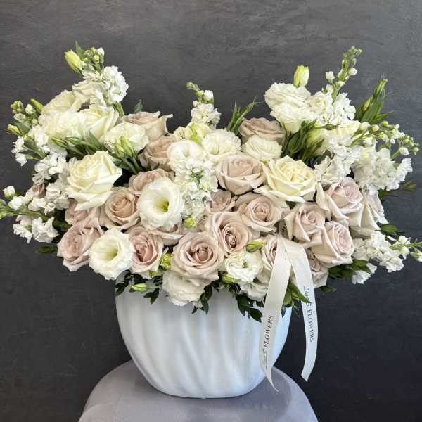 Cream and blush rose arrangement in a white vase with a ribbon