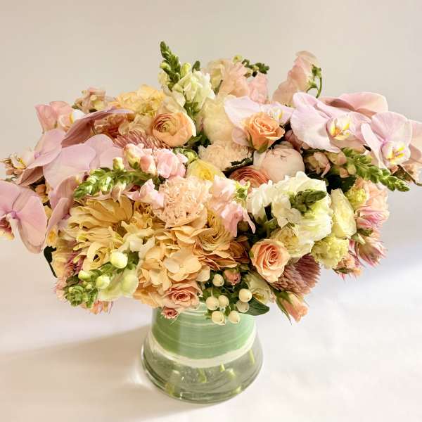 Pastel bouquet of orchids, roses, and mixed blooms in a glass vase