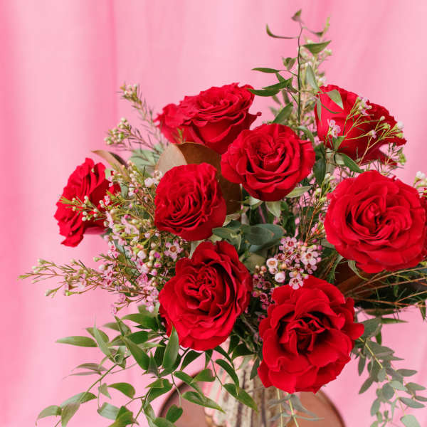 Red roses arranged in a gold vase with airy filler flowers