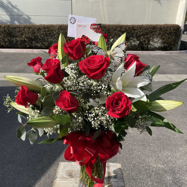 Red roses and white lilies in a glass vase with a red ribbon