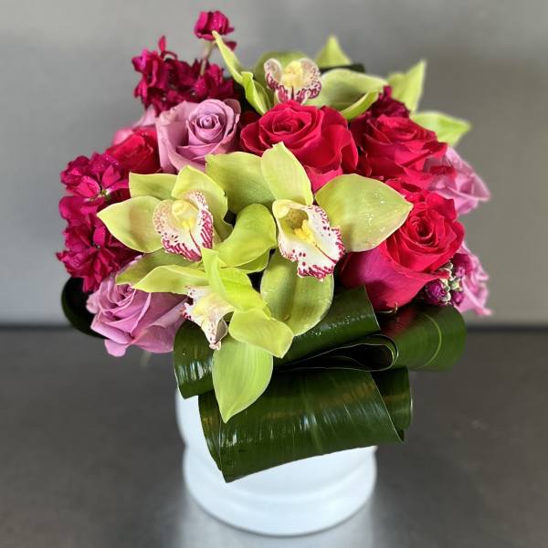 Pink roses and green orchids arranged in a white vase