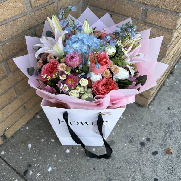Mixed bouquet with pink roses, blue hydrangea, and white lilies in pink wrap