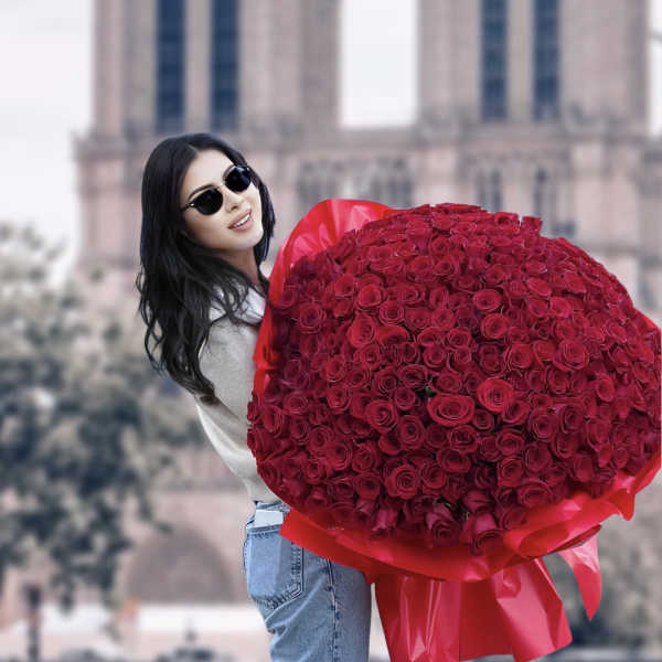 Woman holding a large bouquet of red roses in front of a cathedral