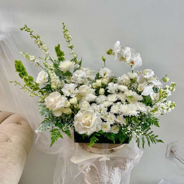 White floral arrangement with orchids and roses in a low container