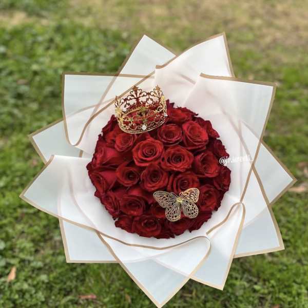 Red rose bouquet wrapped in white paper with a crown and butterfly decoration