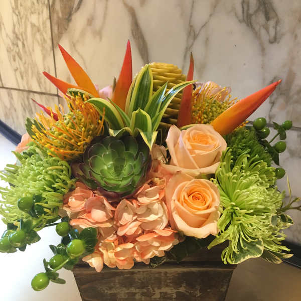 Tropical floral arrangement in a square planter with roses and succulents