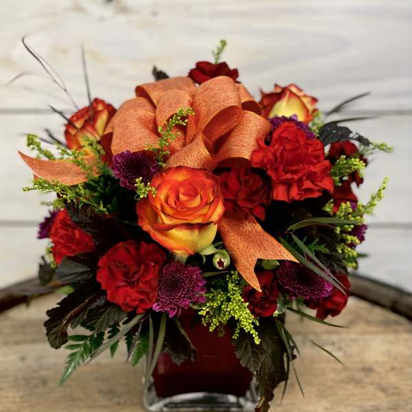 Orange and red rose bouquet in a square glass vase