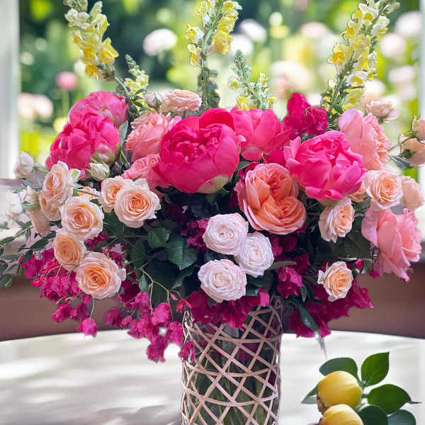 Pink and peach floral arrangement in a glass vase with yellow snapdragons