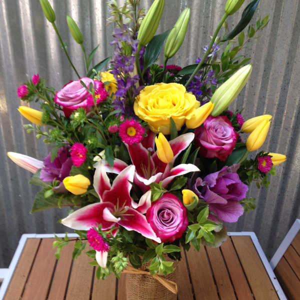 Mixed bouquet of roses, lilies, and tulips in a burlap-wrapped vase
