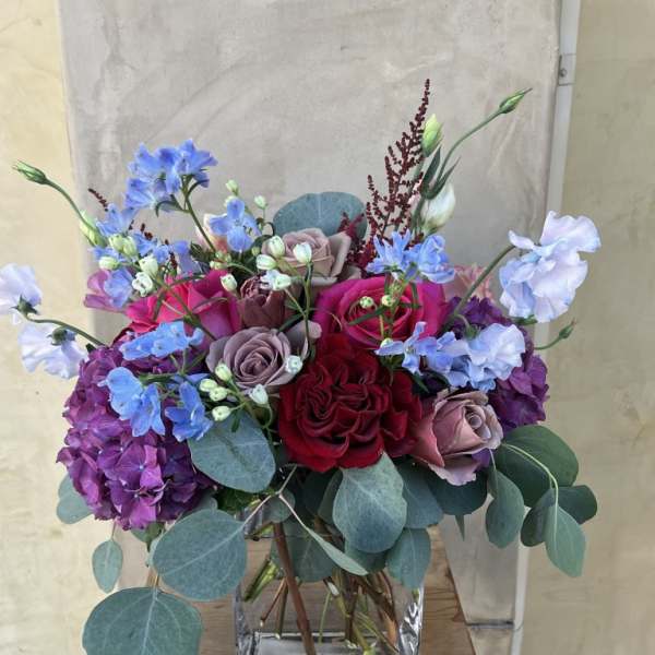 Mixed bouquet of roses, hydrangeas, and blue flowers in a glass vase