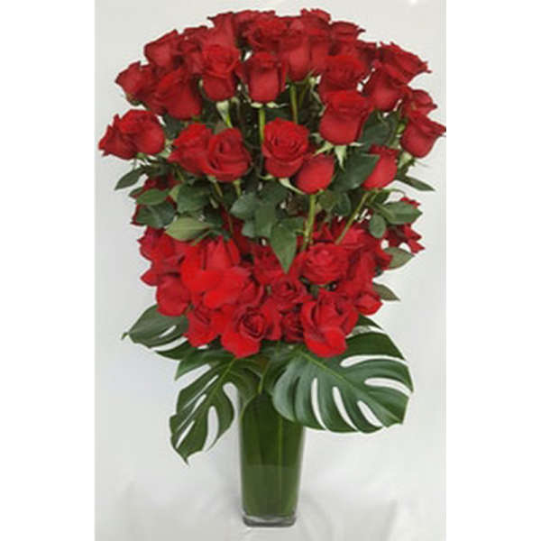 Tall vase arrangement of red roses with large tropical leaves