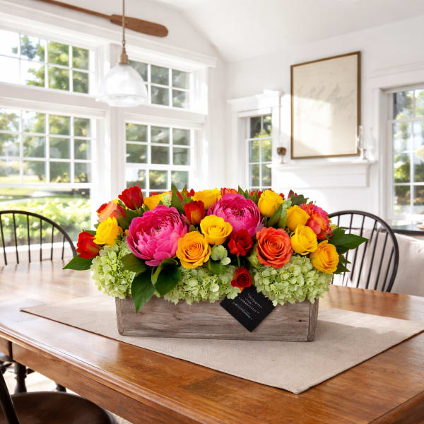 Bright mixed flower arrangement in a wooden box on a dining table