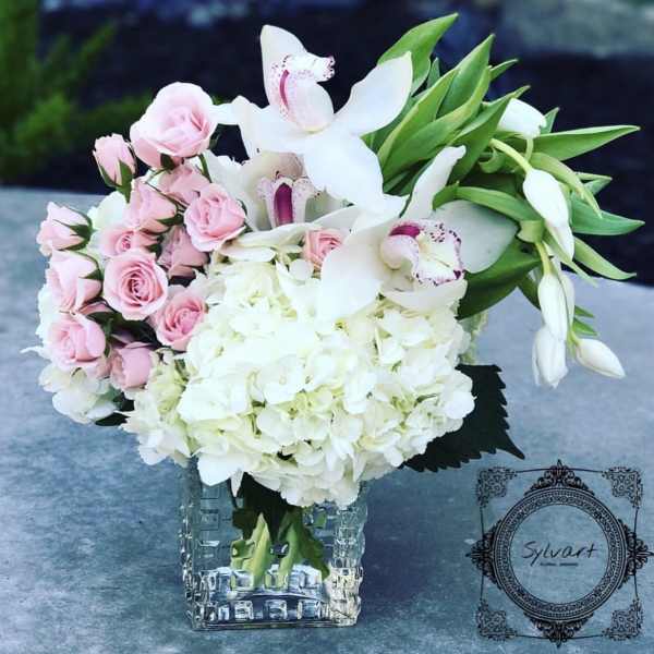 Pink roses and white orchids arranged in a clear square vase