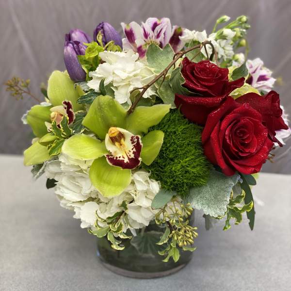 Mixed bouquet of red roses, white hydrangea, and purple orchids in a glass vase