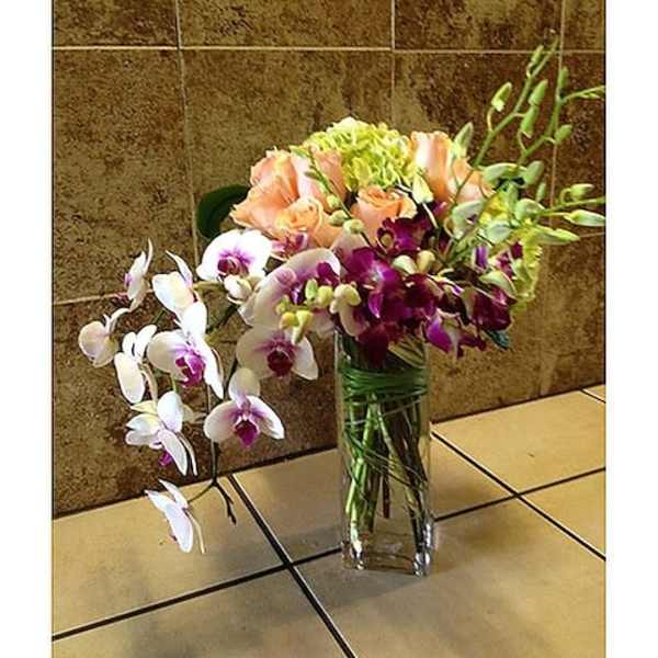 Orchid arrangement in a clear glass vase with peach and white blooms