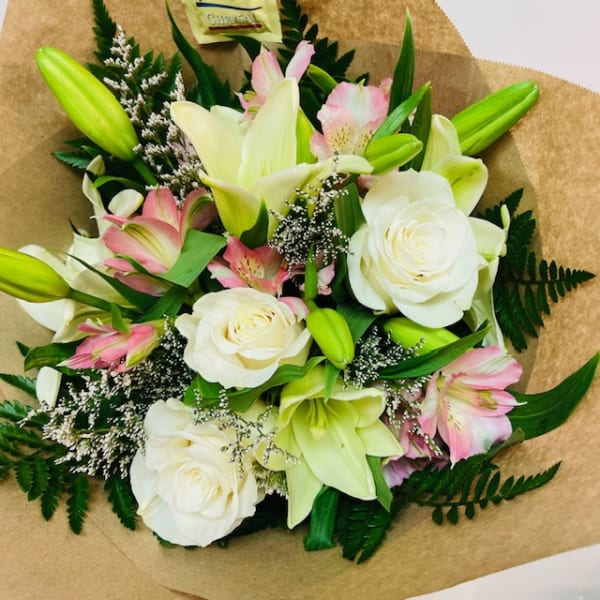 Bouquet of white lilies, white roses, and pink alstroemeria in brown paper
