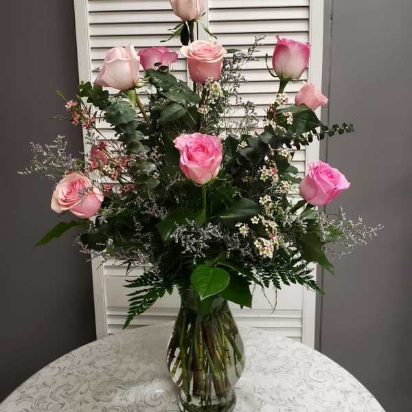 Tall arrangement of light and bright pink roses with delicate white fillers in a clear glass vase