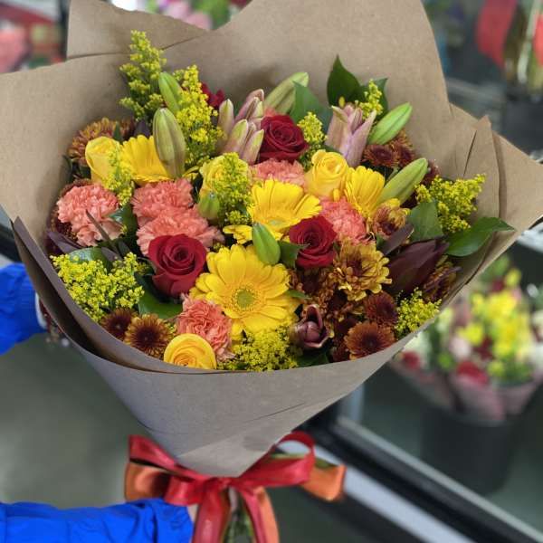 Mixed bouquet of yellow, pink, and red flowers wrapped in brown paper