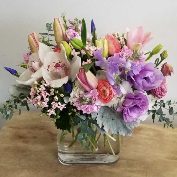 Mixed bouquet of lilies, orchids, and purple blooms in a glass vase