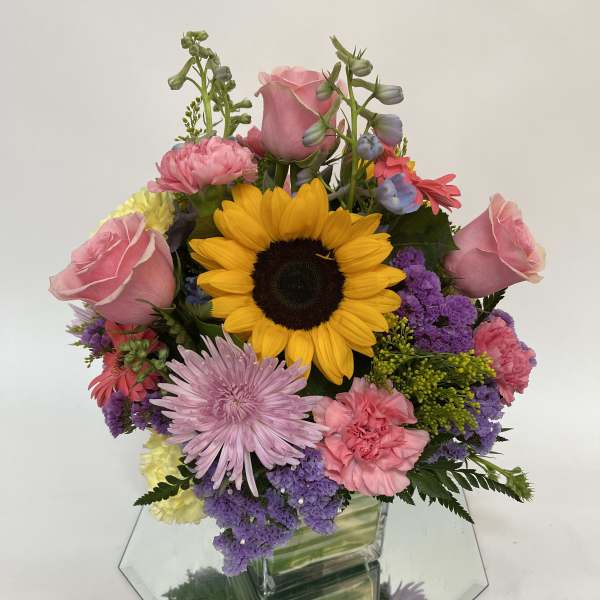 Mixed bouquet with a sunflower, pink roses, and purple flowers in a glass vase