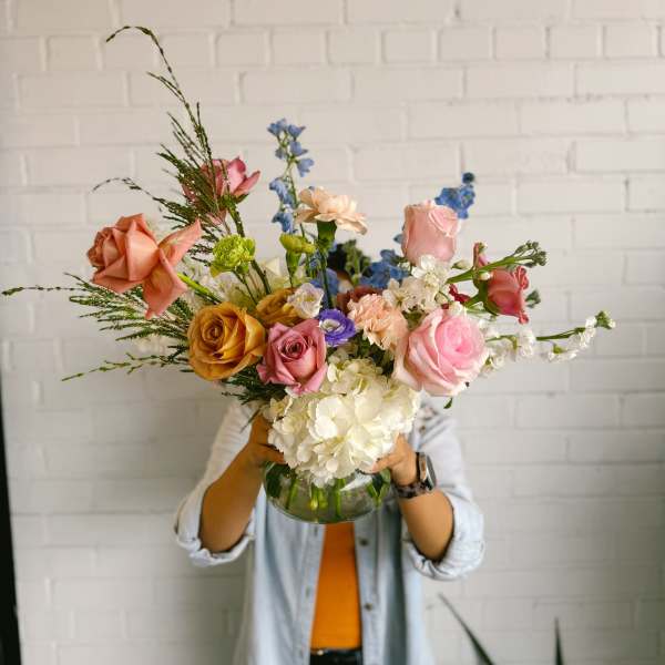 Mixed bouquet of roses, hydrangea, and blue delphinium in a glass vase