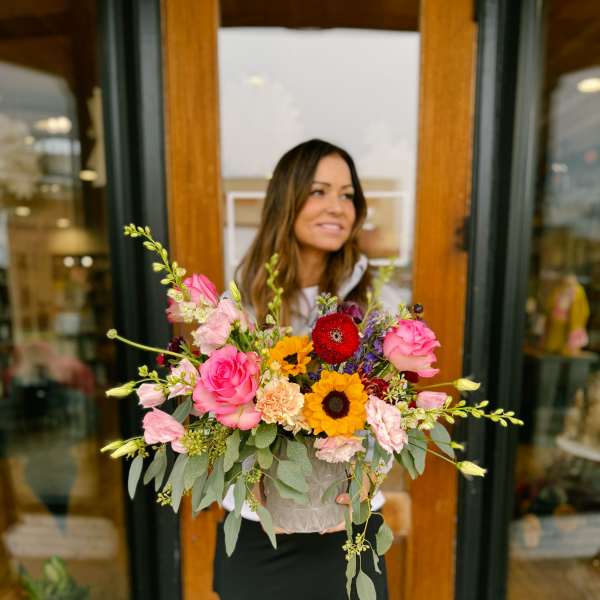 Woman holding a colorful mixed flower arrangement in a textured container