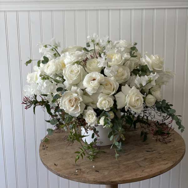White rose arrangement in a white vase with trailing greenery
