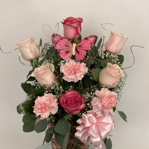 Pink roses and carnations in a glass vase with a butterfly decoration
