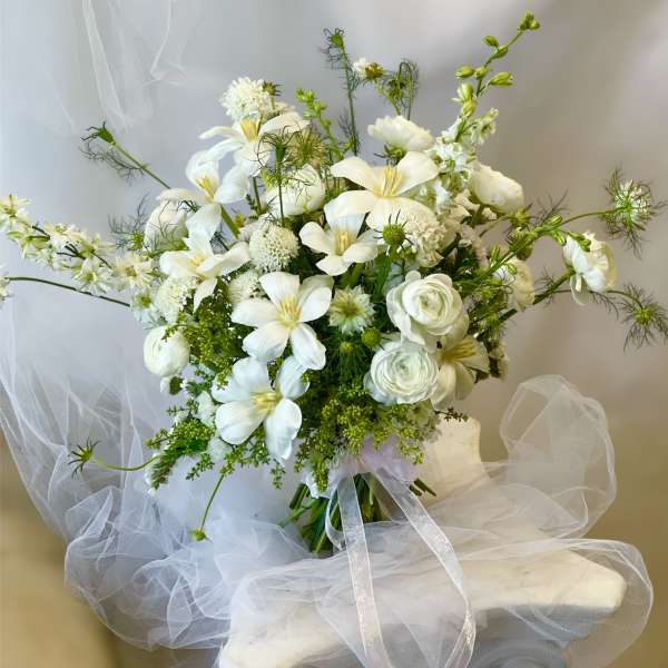 White floral bouquet with lilies and ranunculus tied with a sheer ribbon