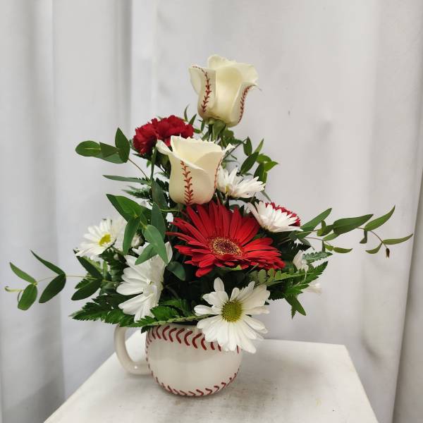 Red and white flowers arranged in a baseball-shaped mug
