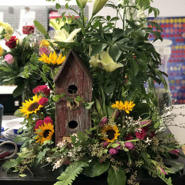 Mixed bouquet with lilies, sunflowers, and roses around a wooden birdhouse