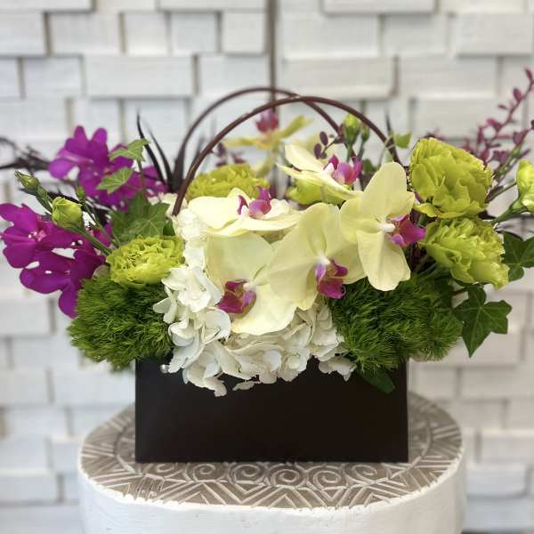 Floral arrangement with orchids, hydrangeas, and green carnations in a dark box