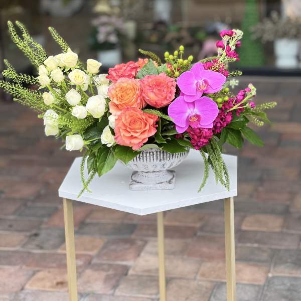Mixed floral arrangement with roses, orchids, and pink blooms in a white pedestal vase