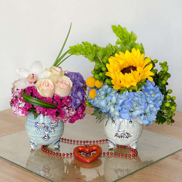 Two colorful floral arrangements in painted ceramic pots with a heart decoration