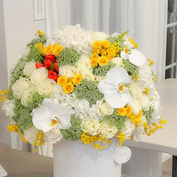 Large white floral arrangement with yellow and red roses in a white hatbox