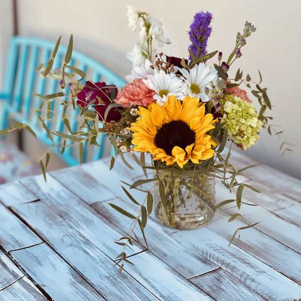 Mixed bouquet with a sunflower in a glass vase on a blue table
