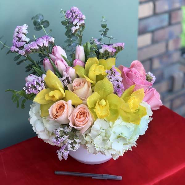 Bouquet of pink roses, yellow orchids, and white hydrangeas in a white vase