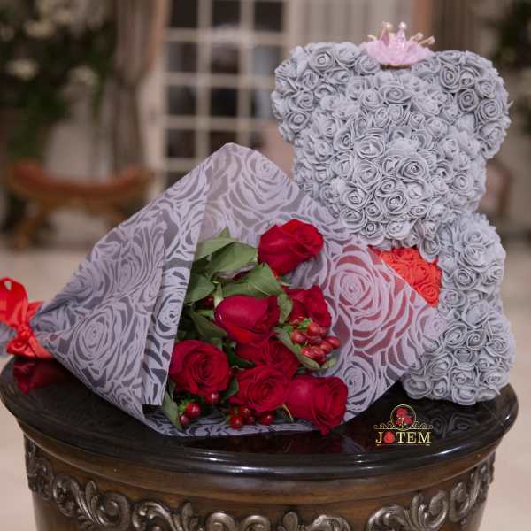 Gray teddy bear made of roses beside a bouquet of red roses
