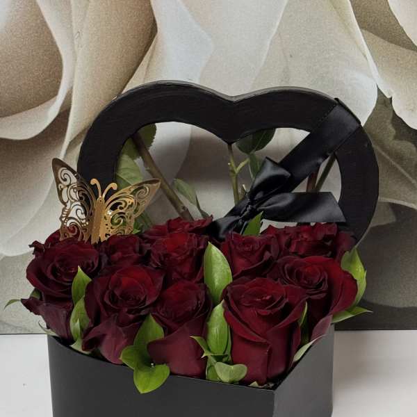 Red roses in a black heart-shaped gift box with a butterfly pick