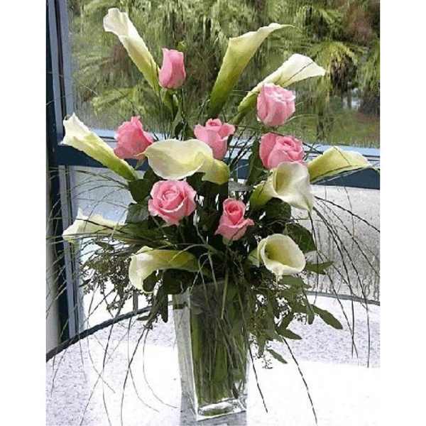 Pink roses and white calla lilies in a tall glass vase