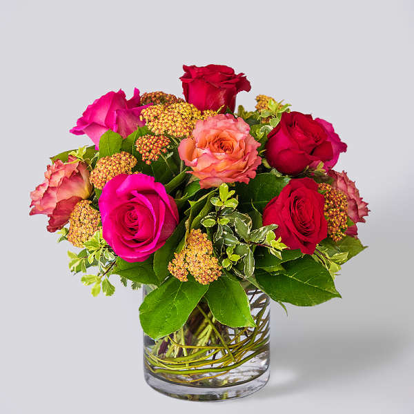 Bouquet of pink and red roses with orange blooms in a clear glass cylinder vase