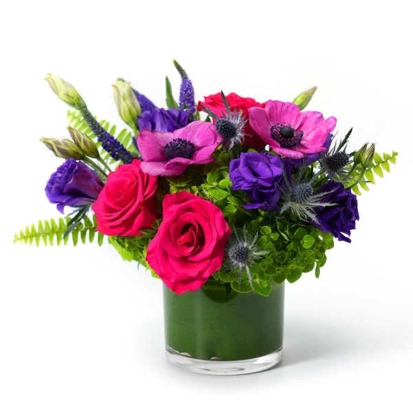 Low glass vase with hot pink roses, magenta anemones, purple flowers, and bright green blooms.
