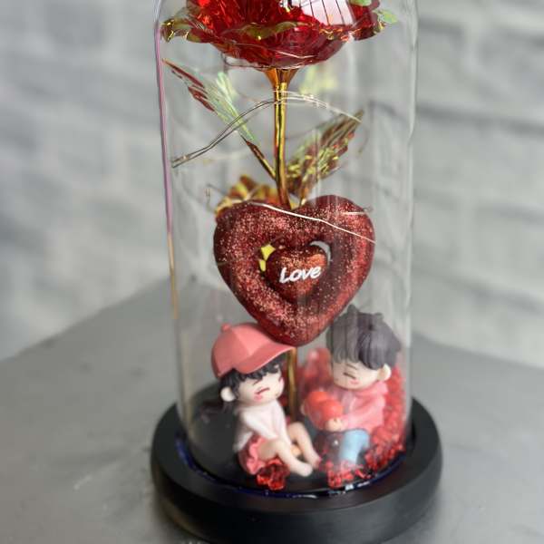 Red decorative rose under a clear dome with two small figurines at the base