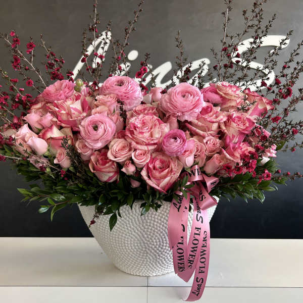 Pink roses and ranunculus in a white textured vase with a pink ribbon