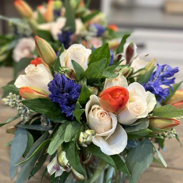Bouquet of white roses, orange tulips, and blue hyacinths in a glass vase
