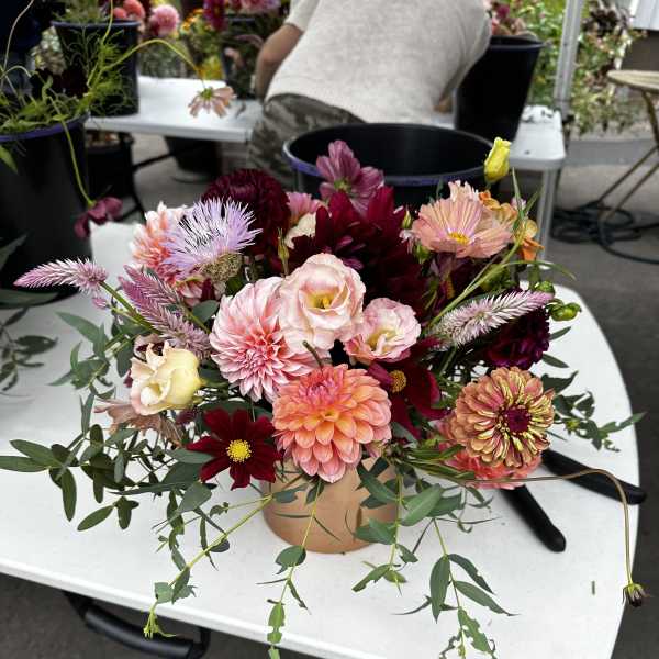 Mixed bouquet of pink, peach, and burgundy flowers in a round container