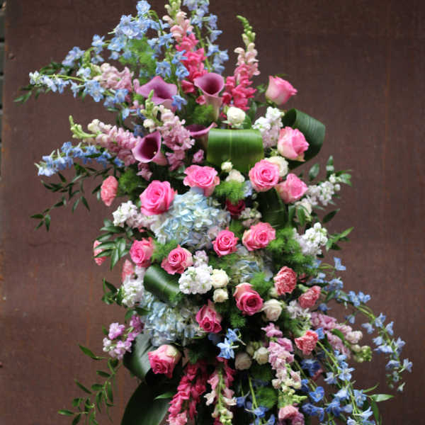 Tall floral standing spray with pink roses, blue delphinium, and purple calla lilies